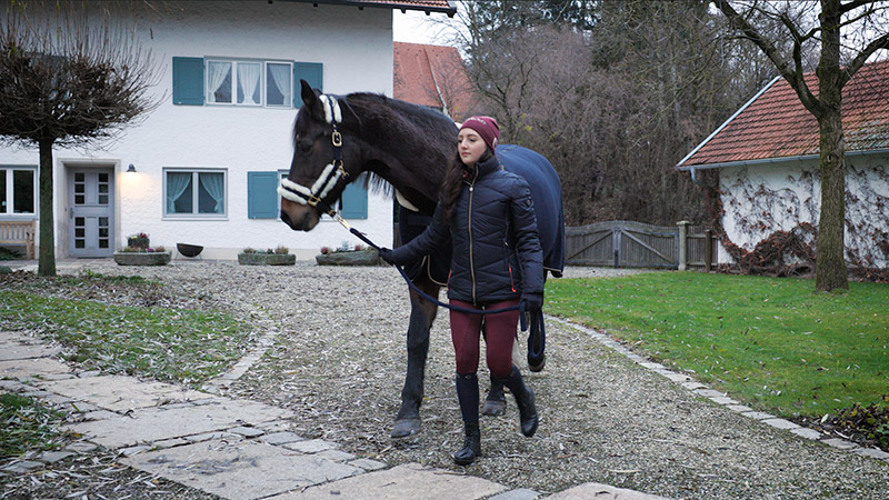 Frau führt ein Pferd über den Hof in Covalliero Reitkleidung