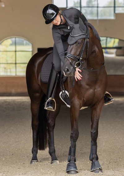 Eine Reiterin in Reitkleidung der Covalliero Anniversary Kollektion auf einem braunen Pferd mit einer Schabracke der Covalliero Anniversary Kollektion