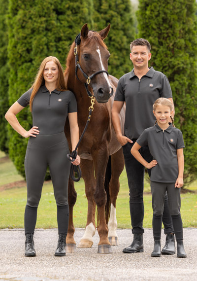Ein braunes Pferd mit einer Frau, einem Mann und einem kleinen Mädchen in Reitsportmode der Covalliero Anniversary Kollektion