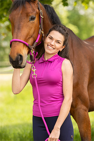 Eine Frau in pinkfarbener Reitbekleidung und Pferd mit pinkem Halfter